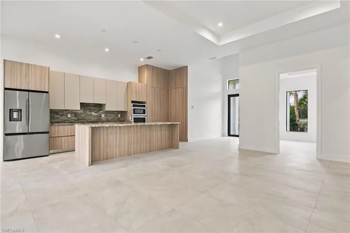 Kitchen featuring flat-panel wood-finish cabinetry, built-in stainless steel appliances, stone-finish backsplash, a large central island, and oversized ceramic floor tile throughout