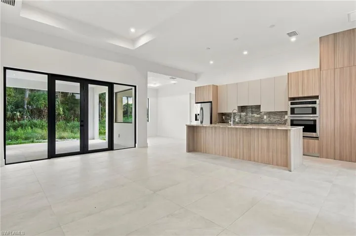 Open-concept kitchen featuring wood-finish cabinetry, built-in double ovens, large stone-patterned island, recessed lighting, and expansive glass multi-panel doors