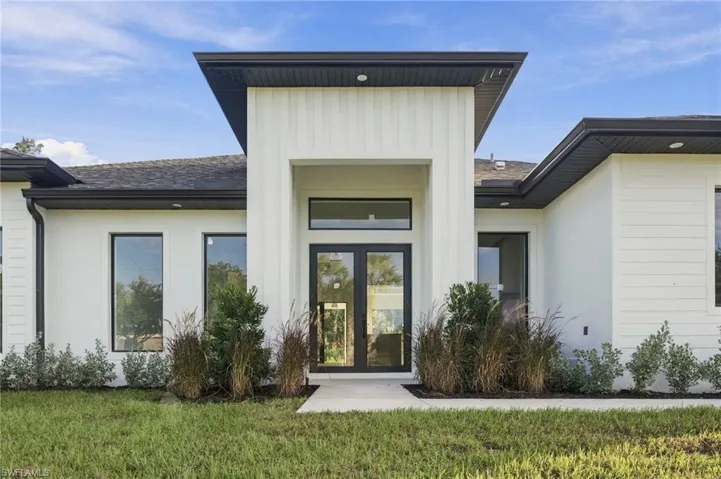 Modern architectural facade featuring vertical and horizontal siding, a prominent covered entryway, dual glass-paneled entry doors, a transom window, and dark contrasting roof trim