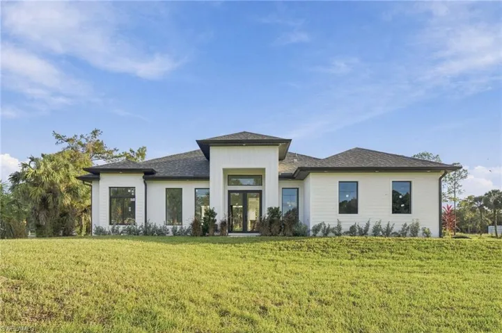 Modern single-story exterior featuring white horizontal siding, a multi-gabled roofline, expansive double-door entry, and black-framed windows