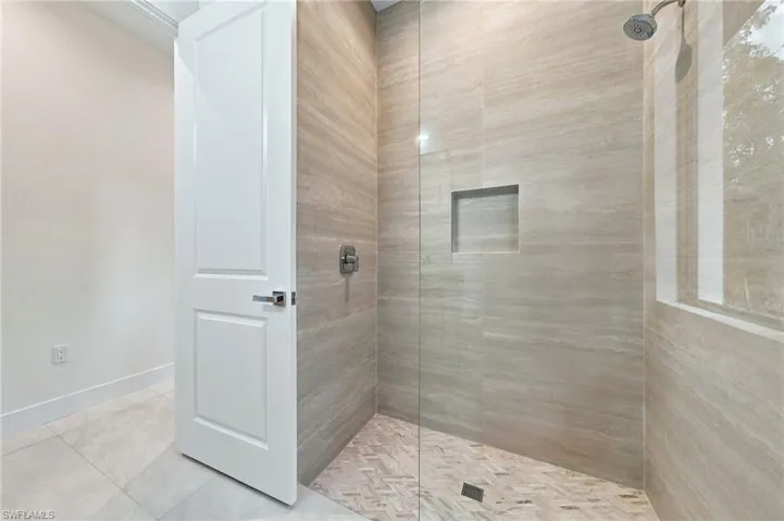 Walk-in shower featuring floor-to-ceiling neutral tile, herringbone-patterned tile flooring, recessed wall niche, and glass enclosure