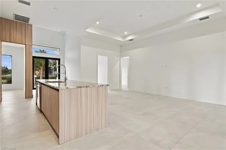 Kitchen featuring a center island with wood-finish cabinetry, stone countertop, and high-arc faucet, complemented by large-format tile flooring and a tray ceiling with recessed lighting