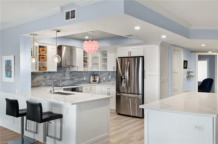 Kitchen with white cabinets, kitchen peninsula, wall chimney exhaust hood, decorative light fixtures, and stainless steel fridge with ice dispenser