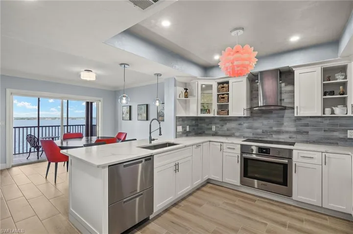 Kitchen with sink, stainless steel appliances, white cabinetry, and wall chimney range hood