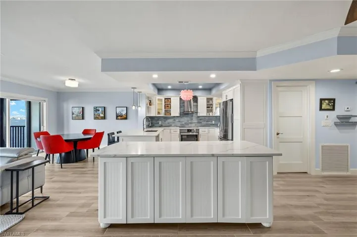 Kitchen featuring stainless steel appliances, wall chimney range hood, light stone counters, pendant lighting, and white cabinets