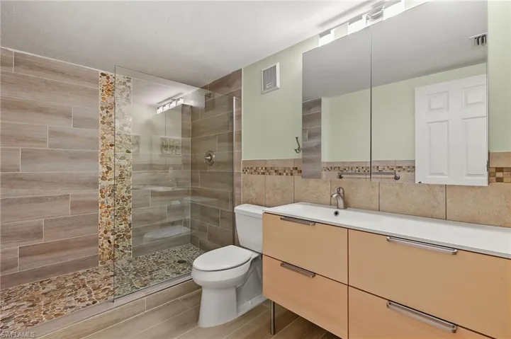 Bathroom with tiled shower, vanity, toilet, and tile walls