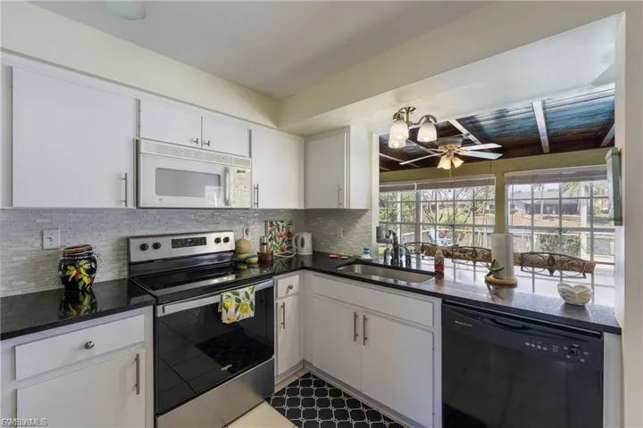 Kitchen with electric range, dishwasher, white microwave, white cabinets, and dark stone counters