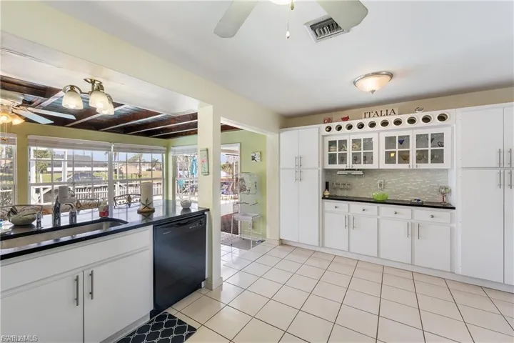 Kitchen with ceiling fan, white cabinets, dishwasher, glass insert cabinets, and tasteful backsplash
