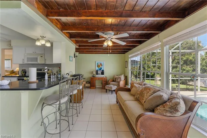 Living area with healthy amount of natural light, ceiling fan, light tile patterned flooring, and a wooden ceiling with exposed beams
