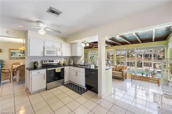 Kitchen featuring stainless steel range with electric cooktop, white microwave, tasteful backsplash, white cabinetry, and black dishwasher
