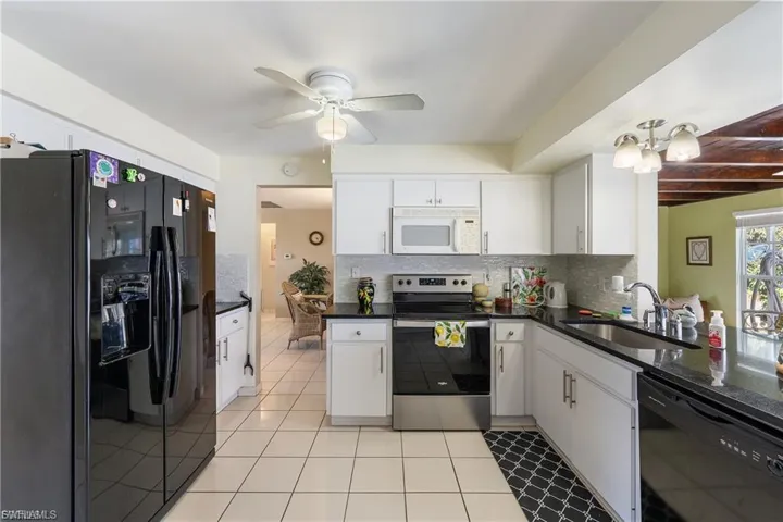 Kitchen with black appliances, ceiling fan, tasteful backsplash, white cabinets, and dark stone countertops