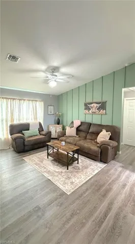 Living room with wood finished floors, a decorative wall, and ceiling fan