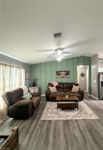 Living room with a decorative wall, a ceiling fan, and wood finished floors