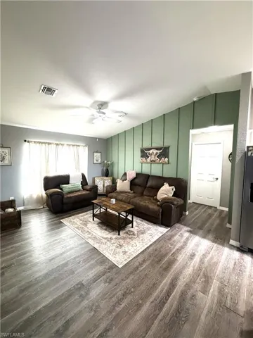 Living room with dark wood-type flooring, ceiling fan, and a decorative wall