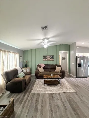 Living room featuring ceiling fan, wood finished floors, and a decorative wall