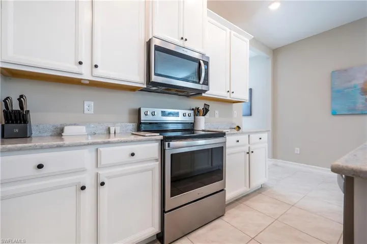 Kitchen with stainless steel appliances, white cabinets, light tile patterned floors, and light stone countertops