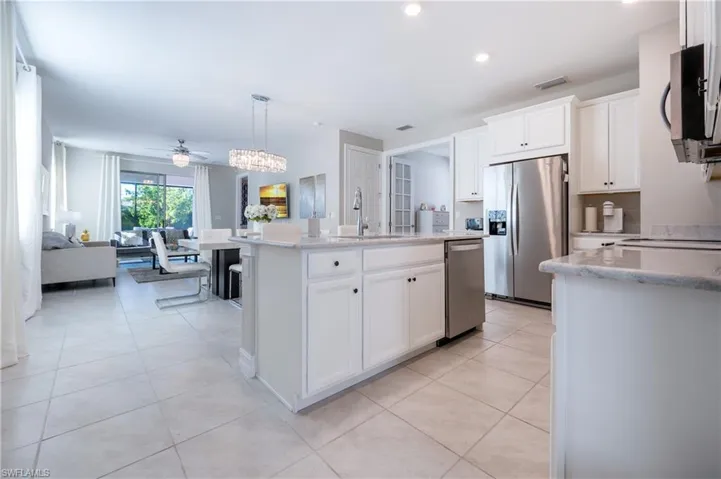 Kitchen featuring white cabinetry, a center island with sink, stainless steel appliances, and light stone counters