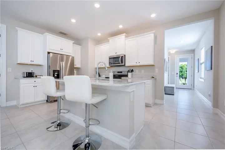 Kitchen featuring a breakfast bar, an island with sink, stainless steel appliances, white cabinetry, and recessed lighting