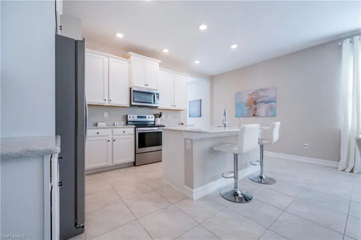 Kitchen with stainless steel appliances, white cabinets, a breakfast bar, a kitchen island with sink, and recessed lighting