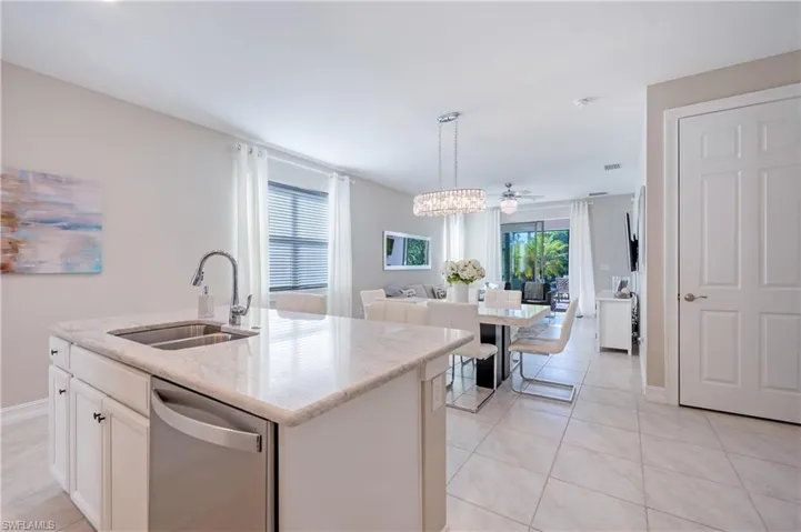 Kitchen with light stone counters, white cabinetry, stainless steel dishwasher, an island with sink, and hanging lights