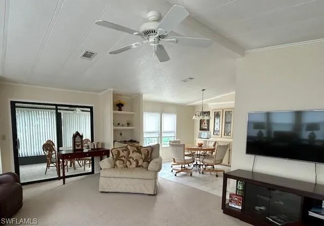 Living area featuring light colored carpet, a textured ceiling, ceiling fan, crown molding, and light tile patterned floors