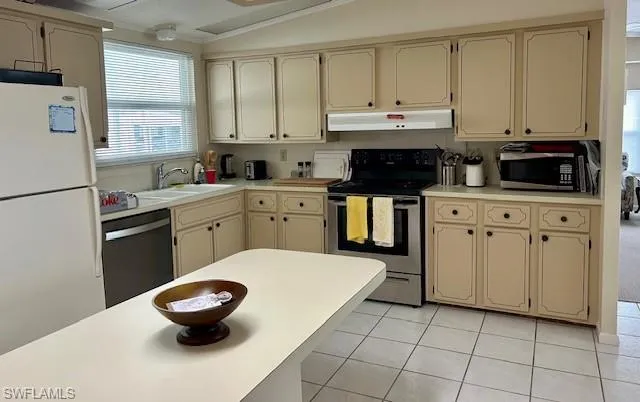 Kitchen featuring stainless steel appliances, light countertops, light tile patterned flooring, lofted ceiling, and under cabinet range hood