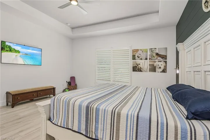 Bedroom with ceiling fan, a raised ceiling, and light wood-type flooring