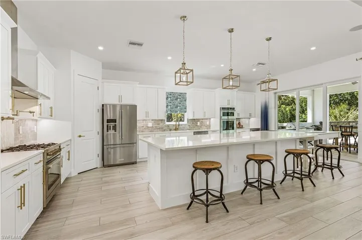 Kitchen featuring decorative light fixtures, a kitchen bar, premium appliances, a large island, and white cabinets