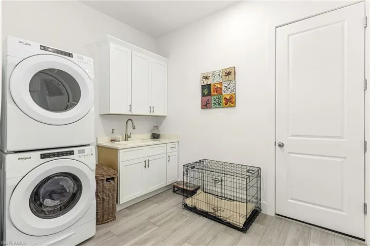 Clothes washing area with stacked washer / drying machine, light wood-type flooring, sink, and cabinets