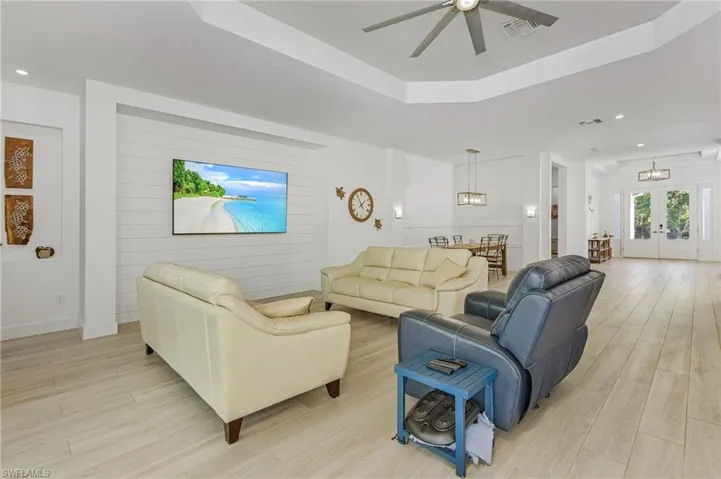 Living room featuring light wood-type flooring, french doors, ceiling fan with notable chandelier, and a raised ceiling