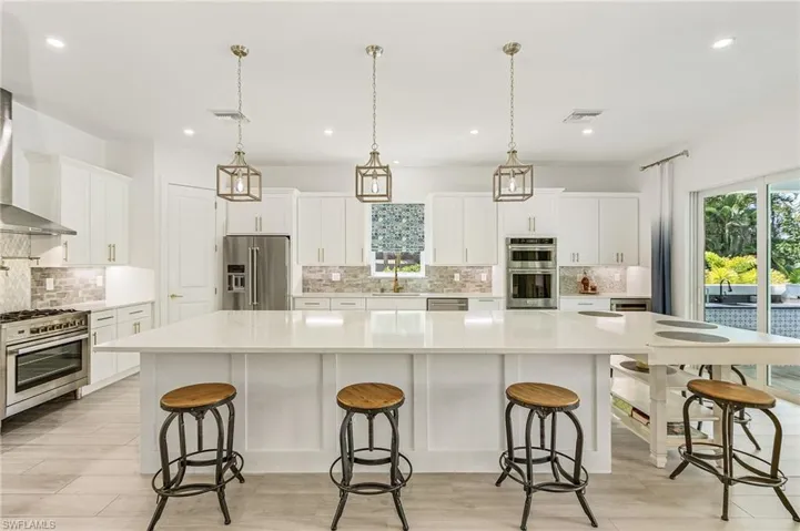 Kitchen with premium appliances, a large island, backsplash, decorative light fixtures, and white cabinets
