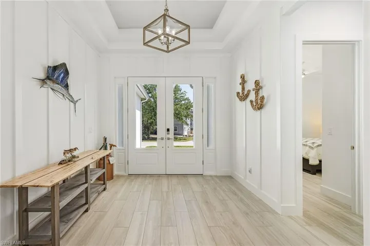 Entryway featuring french doors, ceiling fan with notable chandelier, light hardwood / wood-style flooring, and a raised ceiling