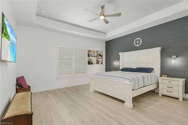 Bedroom featuring ceiling fan, light hardwood / wood-style flooring, and a tray ceiling