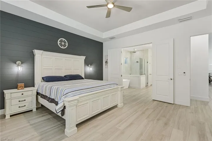 Bedroom with ceiling fan, a high ceiling, connected bathroom, and light hardwood / wood-style floors