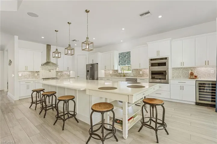 Kitchen featuring beverage cooler, white cabinetry, wall chimney range hood, stainless steel appliances, and a large island