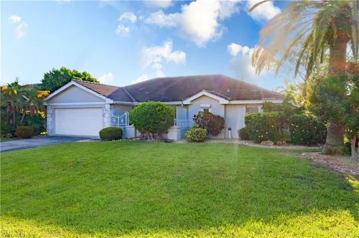Ranch-style home with a tile roof, driveway, a front lawn, and stucco siding
