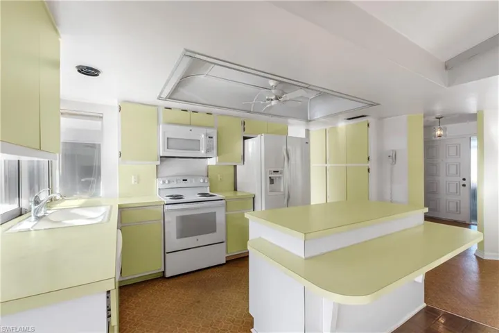 Kitchen with white appliances, a ceiling fan, a center island, and a raised ceiling