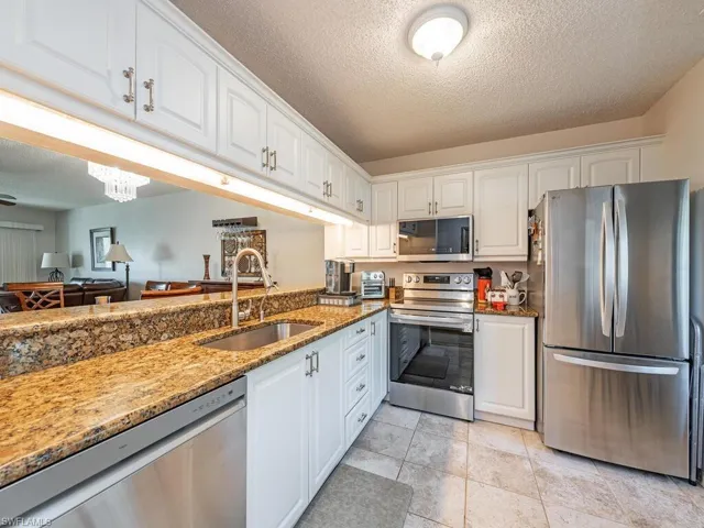 Kitchen featuring white cabinets, light stone counters, stainless steel appliances, a textured ceiling, and a sink