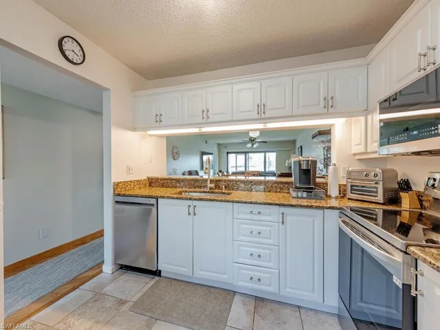 Kitchen with white cabinets, dark stone countertops, stainless steel appliances, and a sink