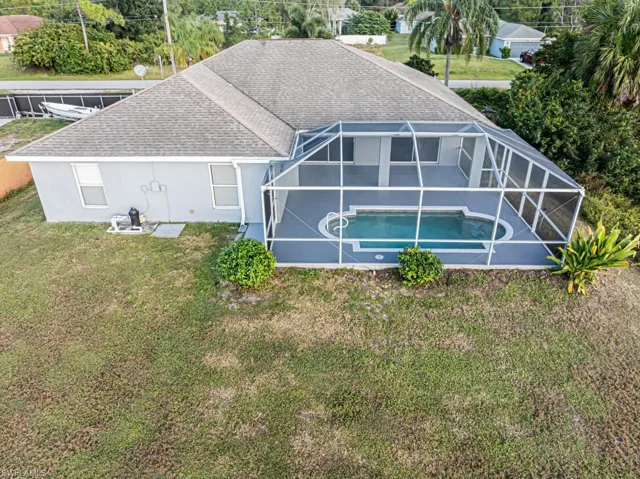 Rear view of house featuring a lanai, a sunroom, a shingled roof, an outdoor pool, and stucco siding