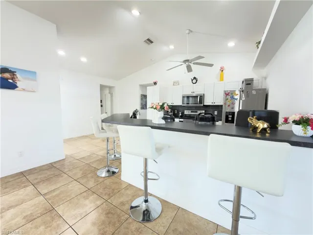 Kitchen featuring a kitchen breakfast bar, white cabinets, stainless steel appliances, dark countertops, and a high ceiling