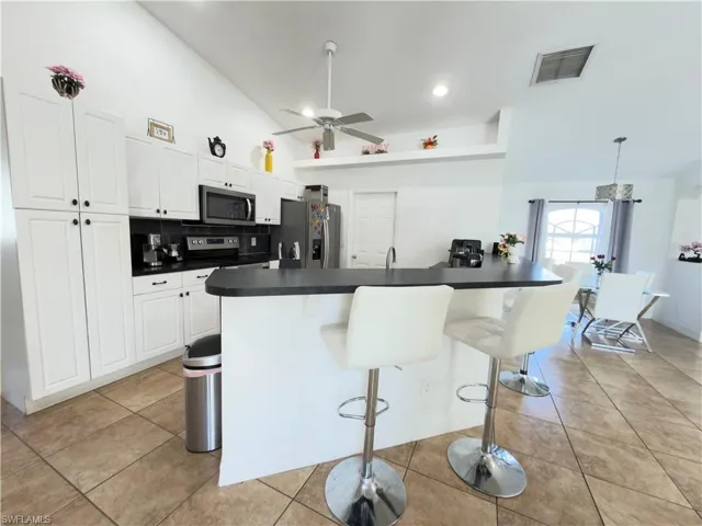 Kitchen with vaulted ceiling, dark countertops, white cabinetry, a kitchen breakfast bar, and stainless steel appliances