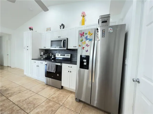Kitchen with stainless steel appliances, white cabinetry, dark countertops, tasteful backsplash, and vaulted ceiling