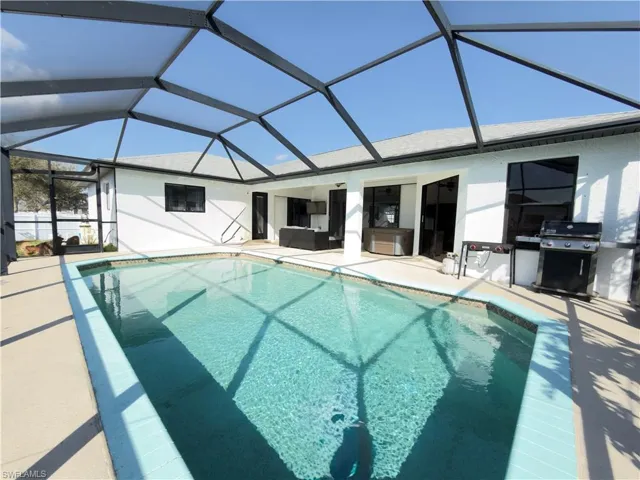 Outdoor pool with a sunroom, glass enclosure, grilling area, and a patio