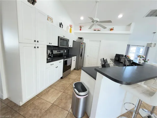 Kitchen with a kitchen bar, a peninsula, stainless steel appliances, white cabinets, and dark countertops