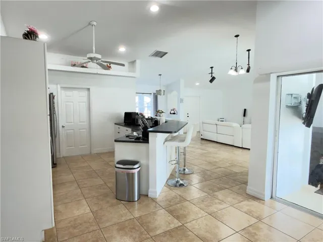 Kitchen featuring a kitchen breakfast bar, dark countertops, a peninsula, a ceiling fan, and decorative light fixtures