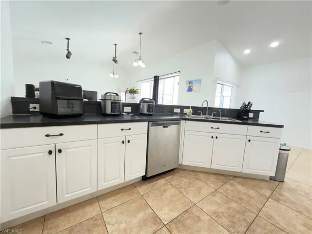 Kitchen with lofted ceiling, white cabinetry, dishwasher, dark countertops, and pendant lighting