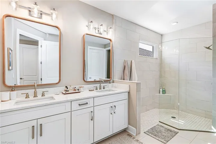 Full bathroom featuring a walk in shower, double vanity, and light tile patterned flooring