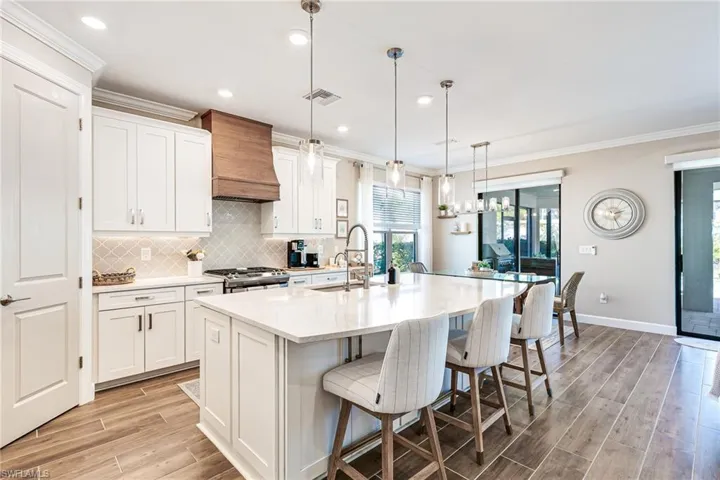 Kitchen with custom wood hood, large island & breakfast bar, white cabinetry, pendant lighting