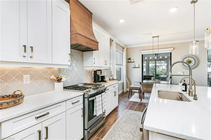 Kitchen with sink in island, stainless steel gas range, light stone countertops